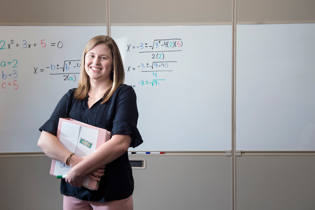 teacher holding books in front of whiteboard